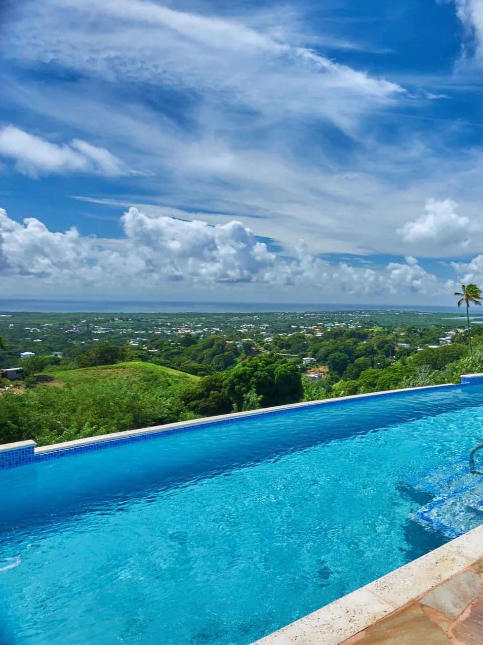 Infinity pool edge looking out over green hills to the Caribbean horizon